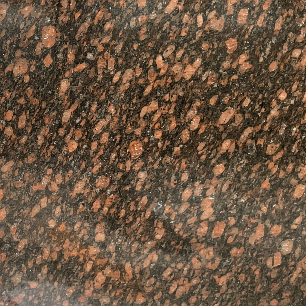 A close-up image of Tan Brown granite, featuring a dark brown to black background with prominent reddish-brown and tan mineral flecks and crystals. This detailed stone texture showcases the natural beauty and durability of the material, ideal for memorial designs.