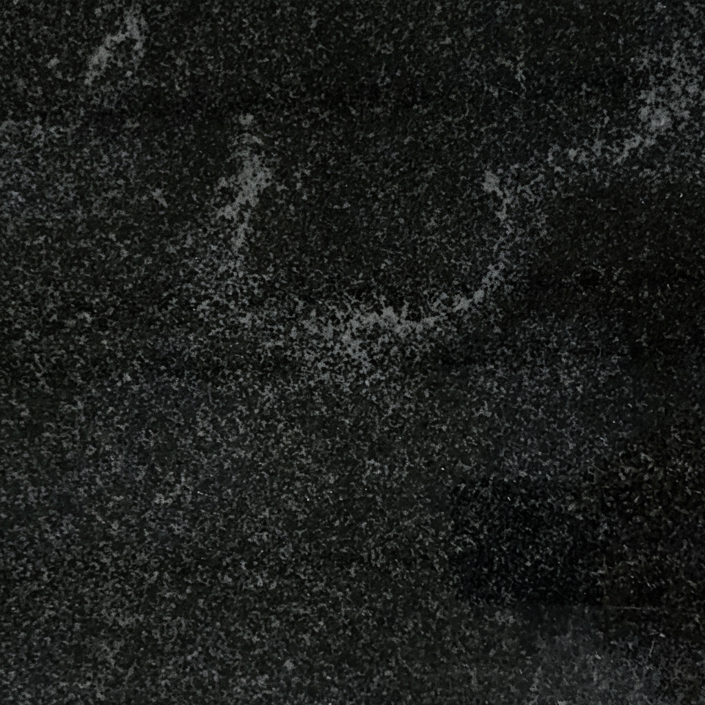 A detailed close-up of a dark granite surface, showing intricate speckles of light gray and black. This natural stone texture provides a durable and dignified aesthetic often chosen for memorial engravings and backgrounds.